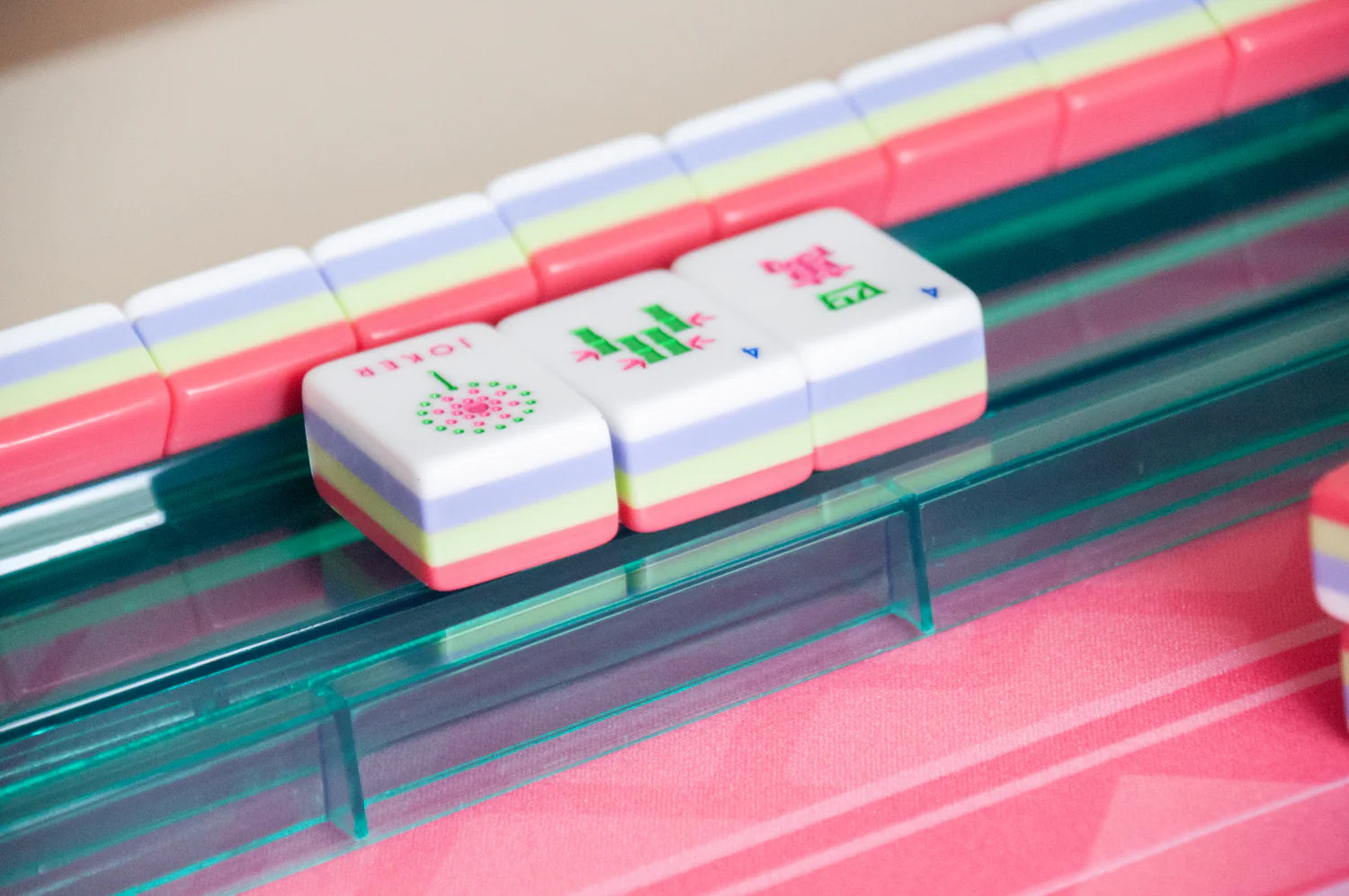 Three pink and green mahjong tiles sitting on a green platform on the side of a hot pink Mahjong game mat.