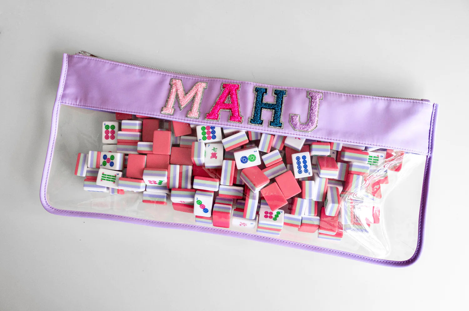 purple and clear zippered bag  with the letters MAHJ in light pink, hot pink,  blue and purple filled with mahjong tiles.