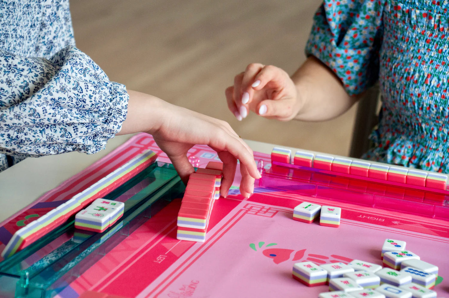 Two people playing the game Mahjong with various mahjong tiles on a pink and hot pink mahjong game board.