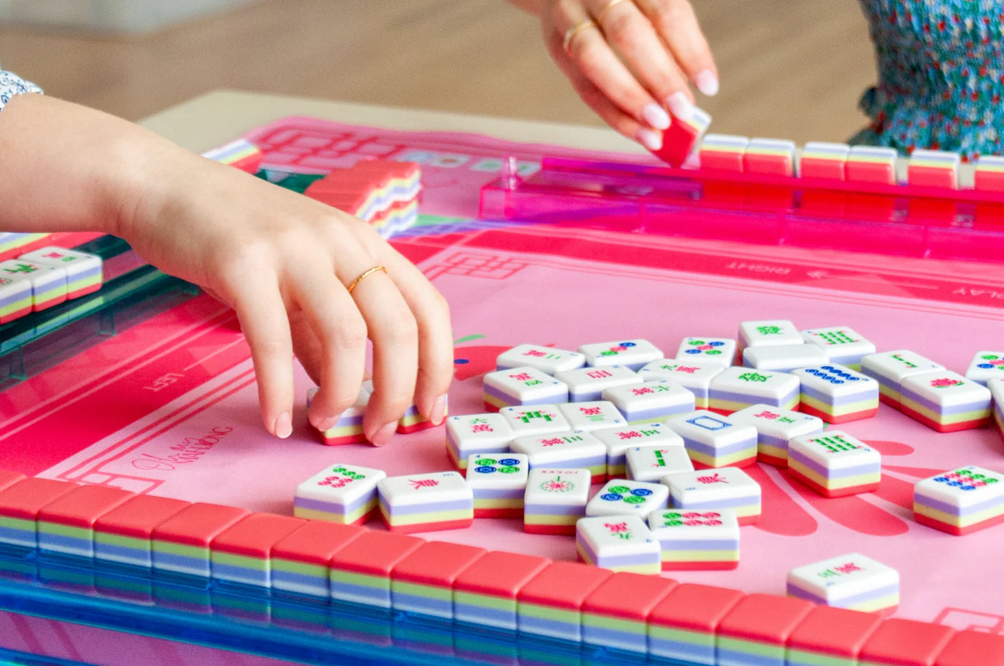 Two people playing the game Mahjong with various mahjong tiles on a pink and hot pink mahjong game board.