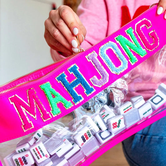 A woman opening a zippered Hot Pink lined clear bag filled with Mahjong tiles with colorful letters reading MAHJONG.