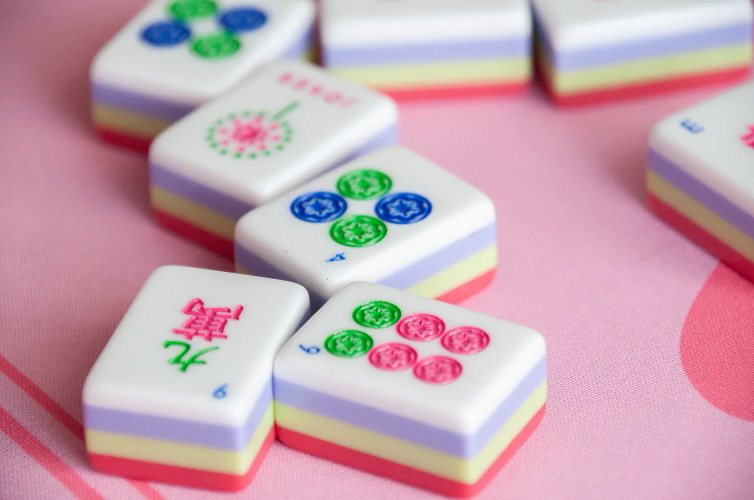 4 Mahjong tiles with pink, green and blue sitting on a pink Mahjong game board.
