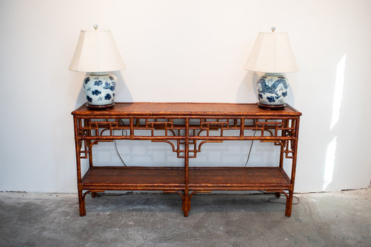 Faux Bamboo Console Table against a white wall with a blue and white lamp with white shade on either side of the table.