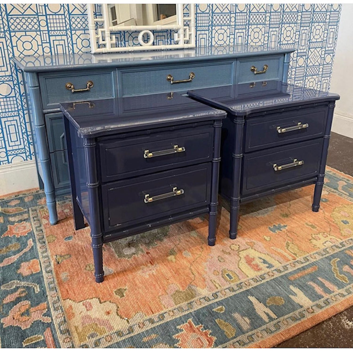 Custom lacquered faux bamboo dresser lacquered in light blue and pair of lacquered side tables in hale navy. All by Winston's Collection located in Winston Salem, NC. All three custom pieces are sitting on a colorful vintage rug with a faux bamboo mirror lacquered in white resting against  a blue and white wallpapered wall.