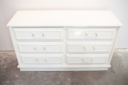 Faux bamboo dresser lacquered in white with lucite pulls against a white wall on a concrete floor.
