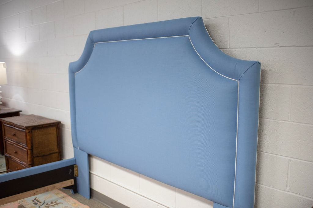 King bed upholstered in blue fabric with white piping