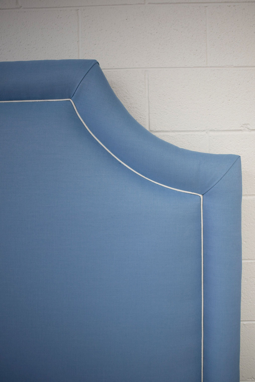 King bed upholstered in blue fabric with white piping